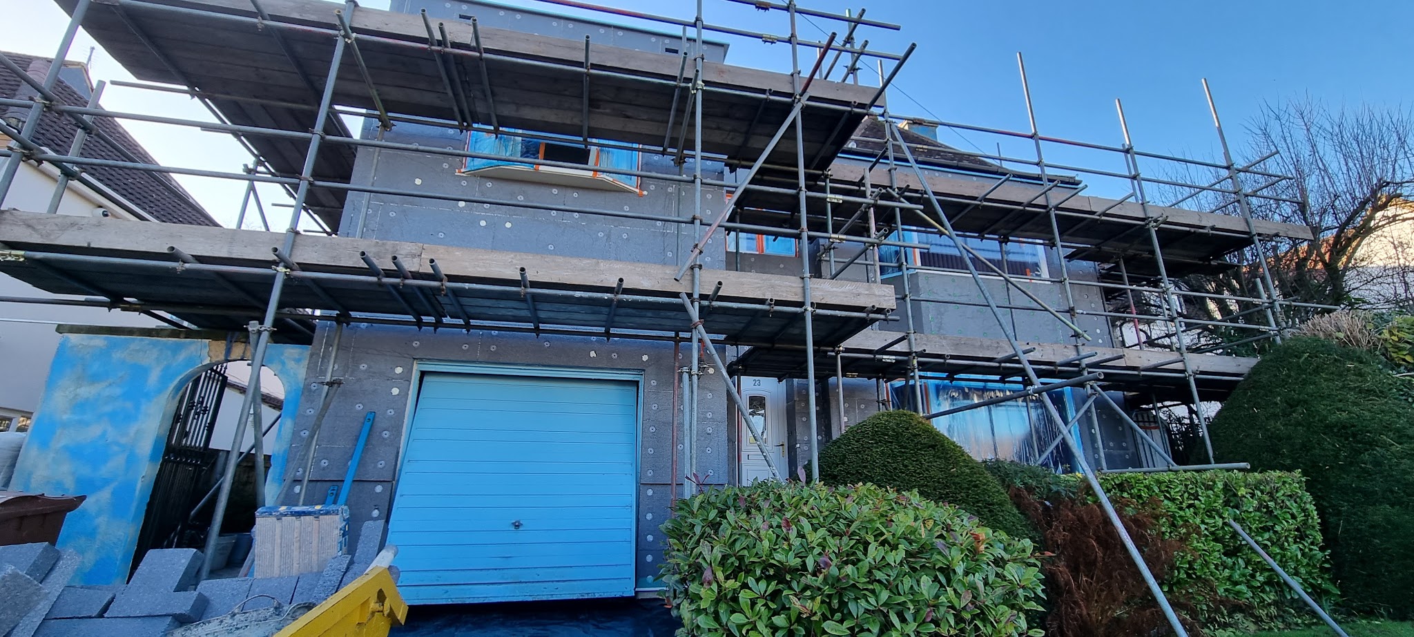 A house exterior prepared for rendering, with scaffolding and masking around windows